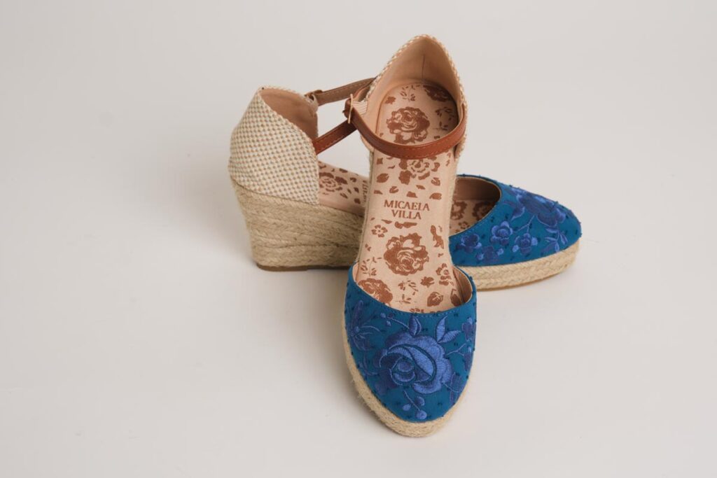Alpargatas de cuña en azul intenso con un refinado bordado floral en la puntera. Este diseño incorpora cierre de pulsera ajustable y una base de esparto, combinando la tradición del calzado flamenco con un estilo moderno y la máxima comodidad para eventos especiales.