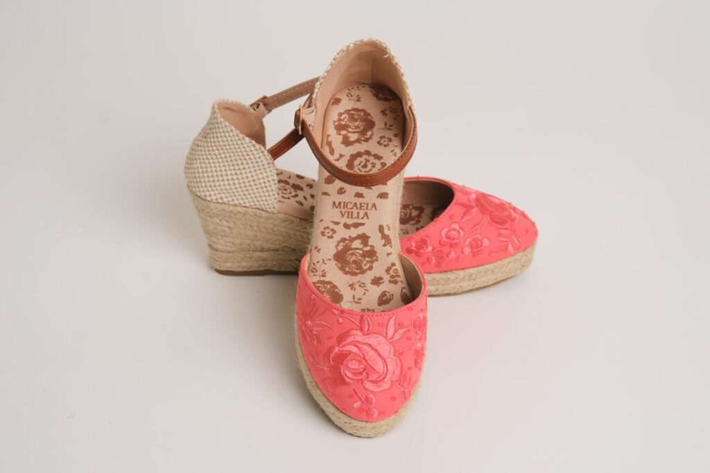 Vibrantes alpargatas de cuña en tono coral, realzadas por un detallado bordado floral artesanal en la puntera. Este modelo, con cierre de pulsera ajustable y base de esparto, aúna la tradición flamenca con un diseño moderno y cómodo, perfecto para completar tus estilismos más alegres.