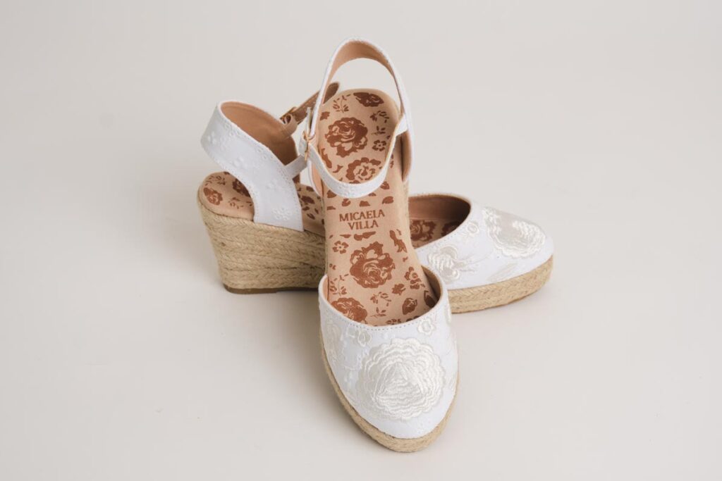 Delicadas alpargatas de cuña en un impecable color blanco, realzadas por un fino bordado floral en la puntera que evoca la pureza de la moda flamenca. Con pulsera ajustable para mayor sujeción y suela de esparto, son el complemento ideal para un look fresco, elegante y sumamente cómodo.