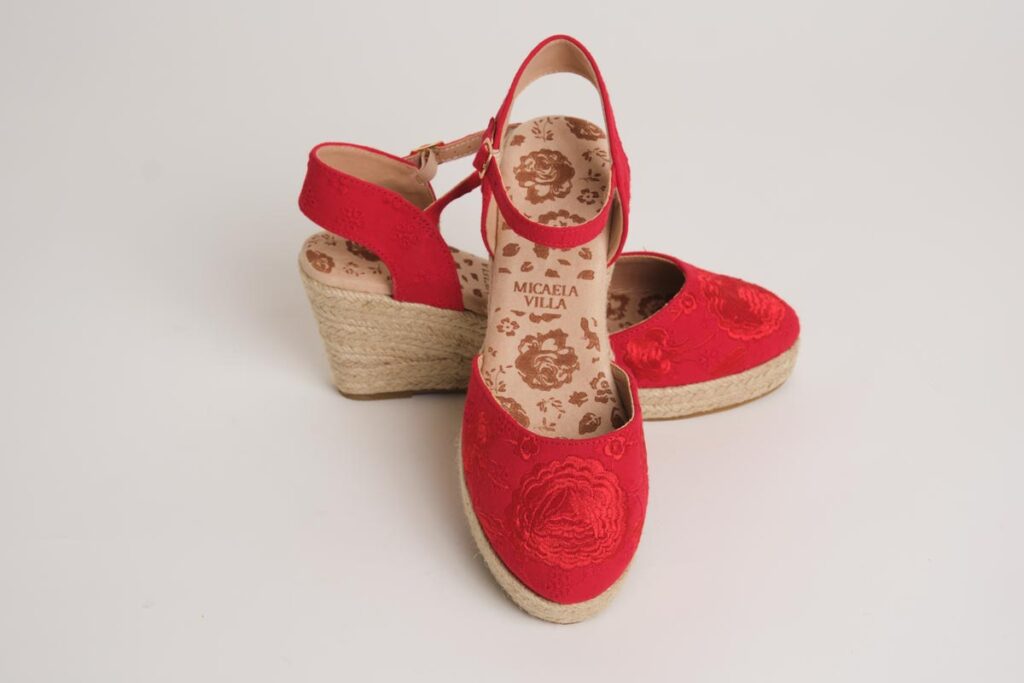Cautivadoras alpargatas de cuña en rojo intenso, destacadas por un intrincado bordado floral que recorre la puntera. Con su diseño de pulsera ajustable y la clásica suela de esparto, ofrecen una combinación perfecta entre estilo flamenco y comodidad para lucir con distinción.