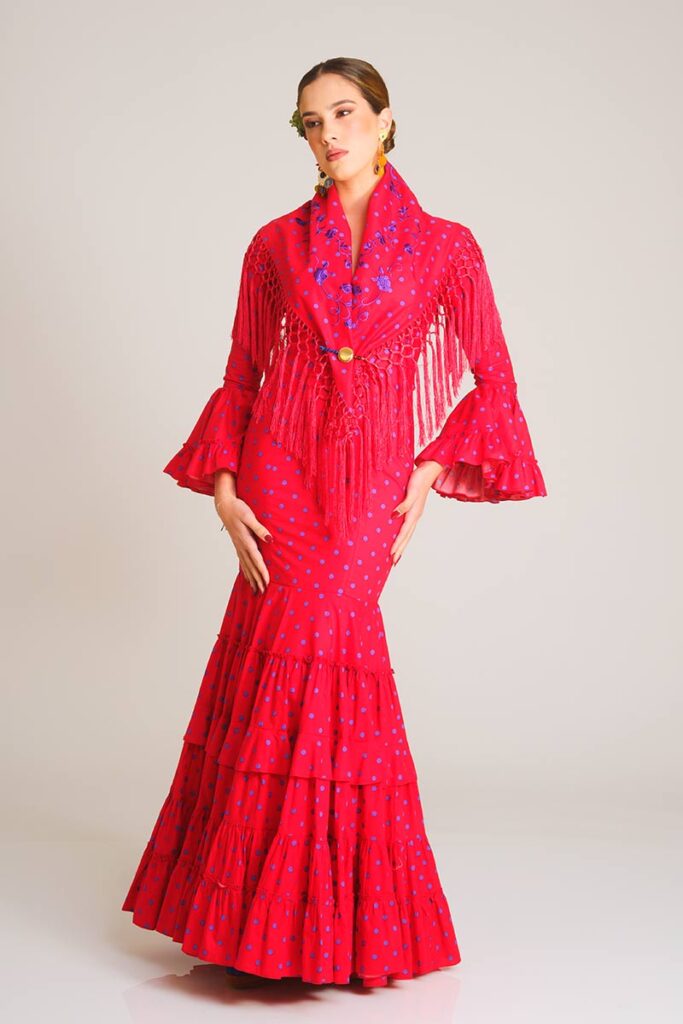 Encantador vestido de flamenca en un intenso tono fucsia con estampado de lunares en contraste. Diseño de corte sirena que estiliza la figura, destacando por su falda de volantes sucesivos que aporta un movimiento fluido y auténtico para tus eventos.
