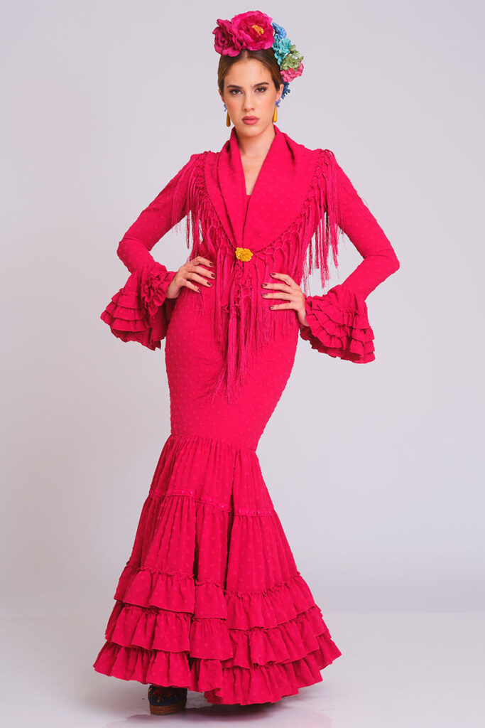 Diseño de flamenca en un vibrante tono fucsia con delicada textura de lunares. Corte sirena que entalla la figura con elegancia, culminando en una falda de volantes sucesivos que brinda un movimiento dinámico y una estética clásica para eventos de moda.