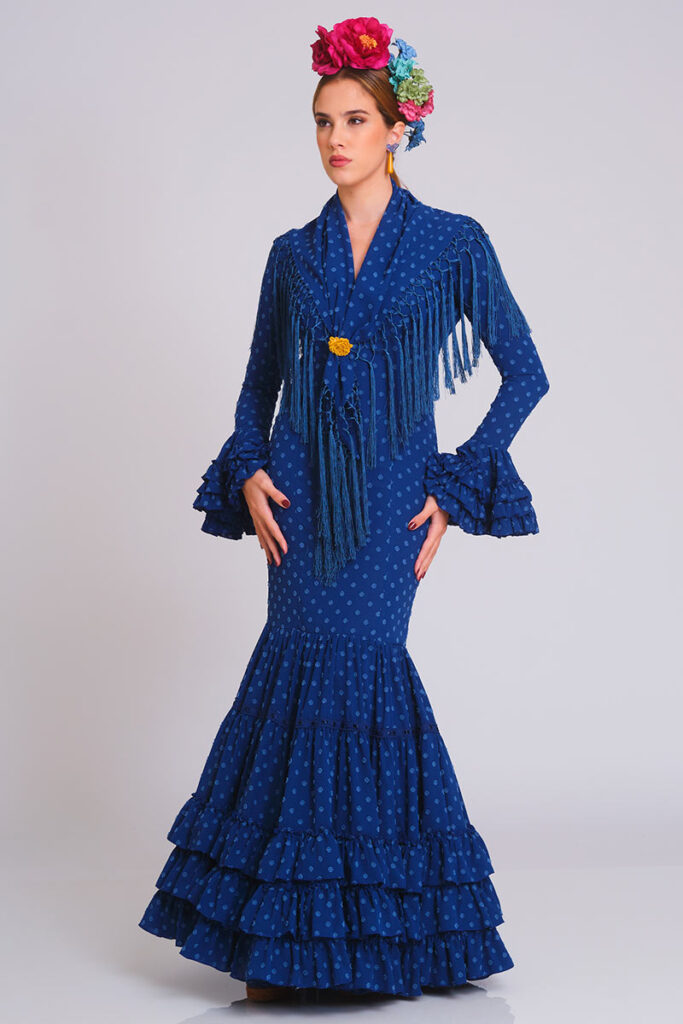 Diseño de flamenca en un intenso tono azul cobalto con sutil textura de lunares. Corte sirena que define la silueta, complementado con una falda de volantes sucesivos que aporta elegancia y movimiento para cualquier evento tradicional.