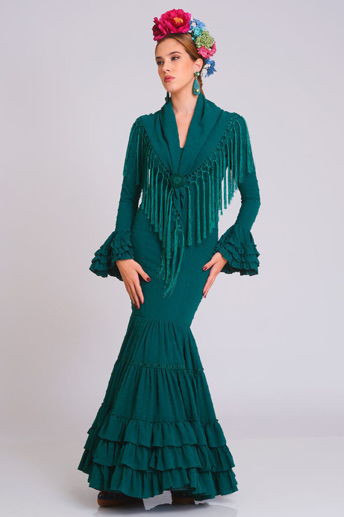 Elegante traje de flamenca en tono verde bosque con sutil textura de lunares. Diseño de corte sirena que entalla la figura, con una falda estructurada en volantes que aporta distinción y movimiento para una estética tradicional y sofisticada.