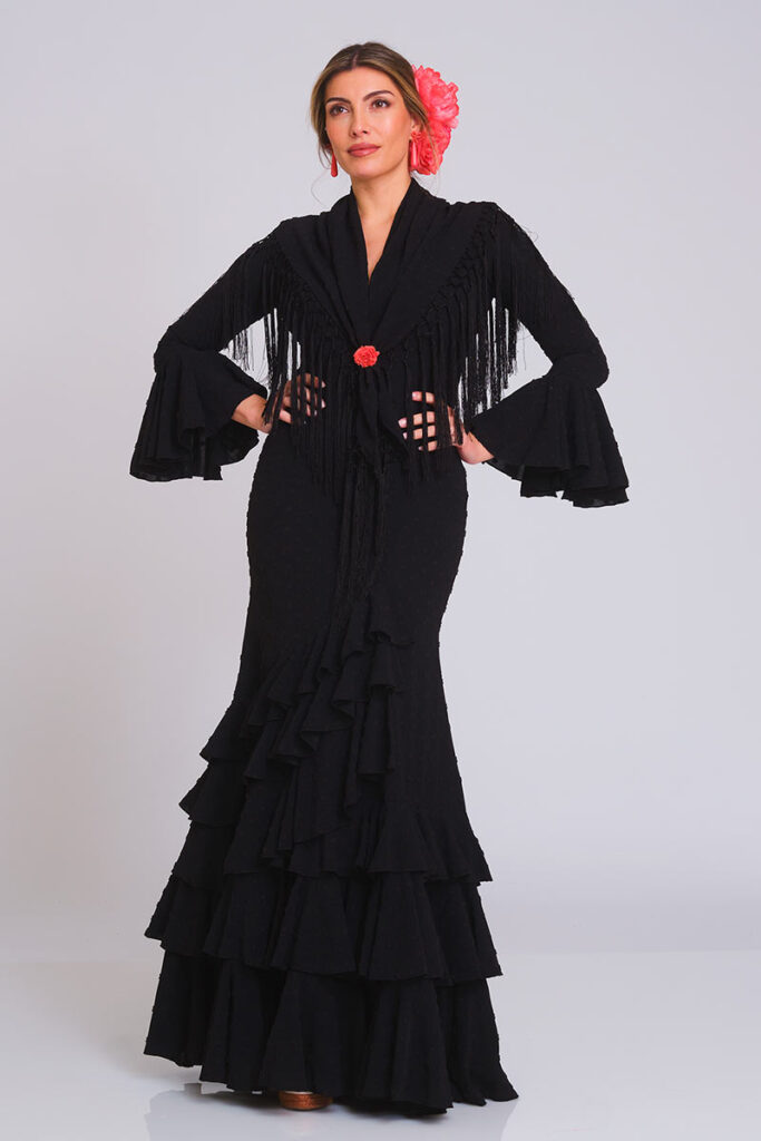 Vestido de flamenca en color negro clásico con una sutil textura de lunares. Presenta un corte sirena que estiliza la figura, con una falda de volantes sucesivos que proporciona un movimiento fluido y una estética elegante y profesional para cualquier evento.
