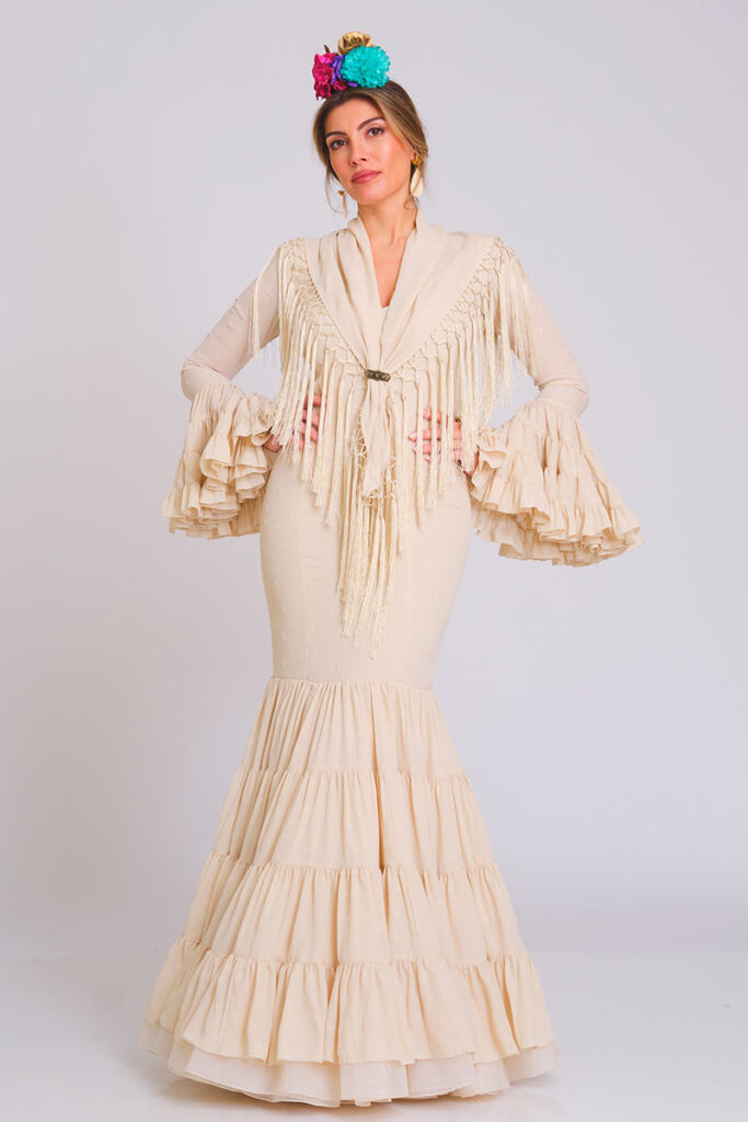 Sofisticado vestido de flamenca en tono crema con sutil textura de lunares. Diseño de corte sirena que estiliza la figura, destacando por su falda estructurada en volantes que aporta elegancia y un movimiento natural para eventos tradicionales.