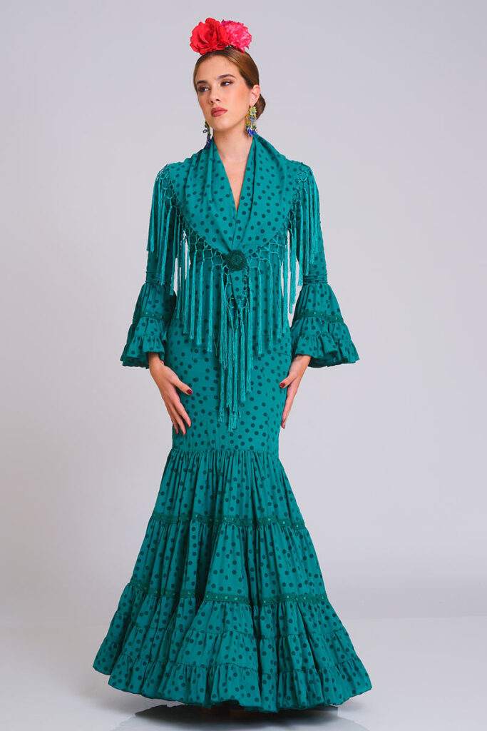 Diseño de flamenca en un vibrante tono verde con estampado de lunares oscuros en contraste. Corte sirena que define la silueta, con una falda estructurada en volantes ribeteados que aporta elegancia y un movimiento excepcional.