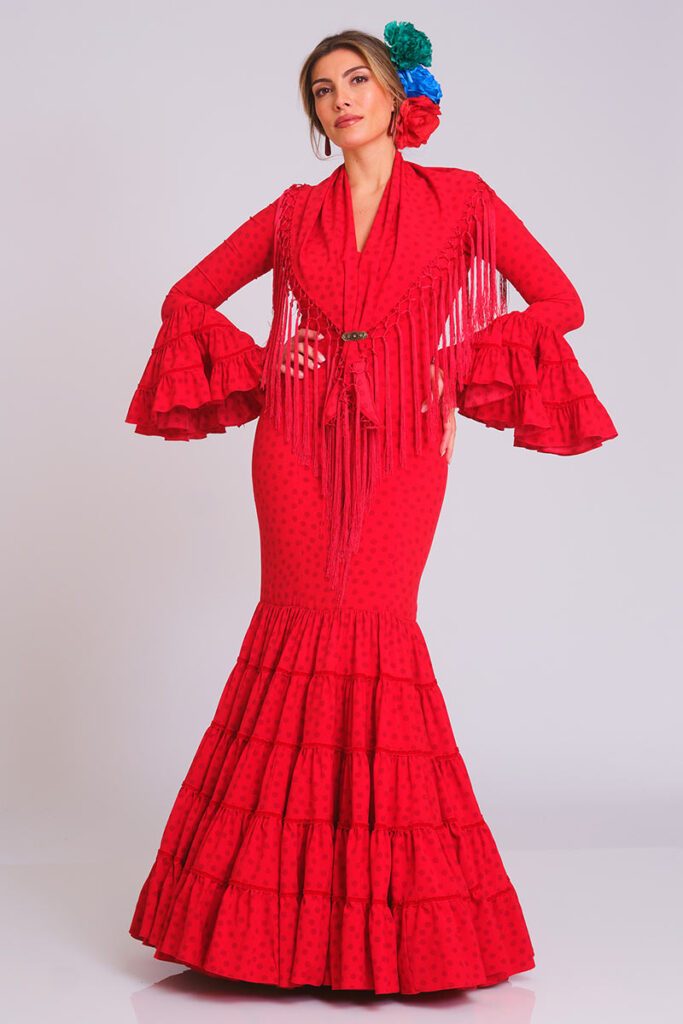 Este deslumbrante vestido de flamenca en un intenso color rojo con sutiles lunares a tono es una elección poderosa y tradicional. Su diseño de corte sirena entalla la figura con elegancia, mientras que la falda, compuesta por múltiples volantes sucesivos, garantiza un movimiento espectacular en cada paso.