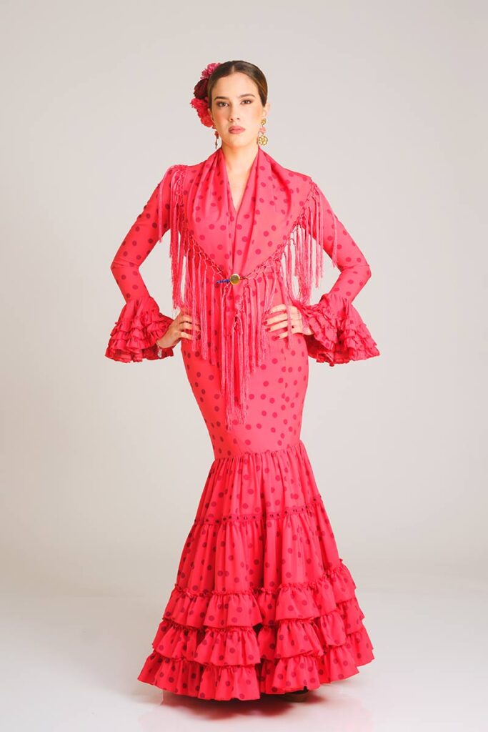 Traje de flamenca de color rosa vibrante con lunares de un tono más oscuro, presentando un diseño de corte sirena entallado y falda con volantes superpuestos para una silueta clásica y estilizada.