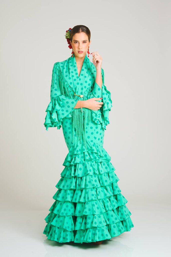 Vestido de flamenca en un brillante tono verde con estampado de lunares, que destaca por un corte sirena que estiliza la figura y una falda formada por múltiples volantes en cascada para lograr una apariencia dinámica y con carácter folclórico.