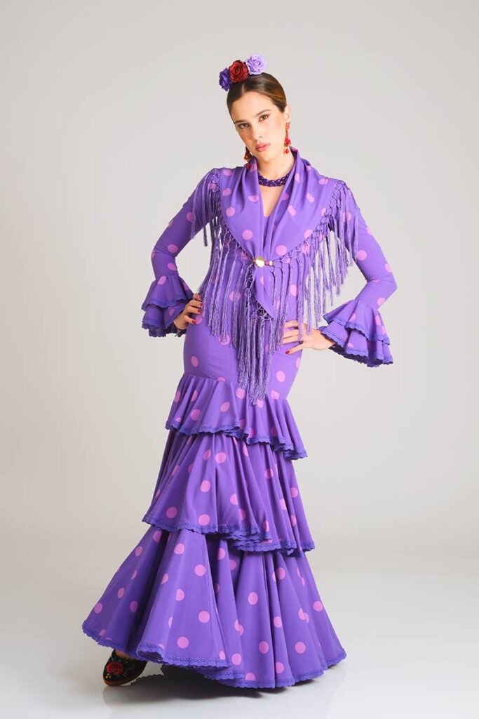Traje de flamenca en un vibrante color morado con lunares en un tono más suave, caracterizado por su corte sirena ajustado y una falda compuesta por capas de volantes que aportan un toque distintivo y folclórico.