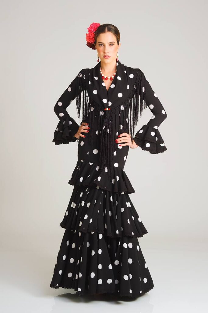 Vestido de flamenca en elegante color negro con estampado de lunares blancos, diseñado con un corte sirena que ajusta la figura y una falda estructurada en volantes superpuestos para ofrecer un acabado clásico y con movimiento.