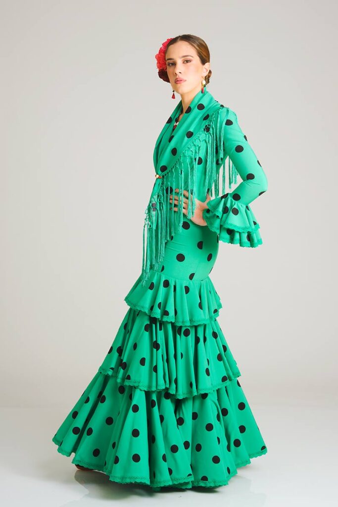 Vestido de flamenca en un vivo color verde con lunares negros, que presenta una silueta entallada tipo sirena y una falda adornada con volantes en capas para lograr un estilo tradicional lleno de vitalidad.