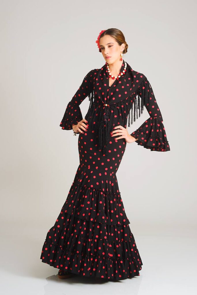 Vestido de flamenca con estampado de lunares rojos sobre fondo negro, confeccionado con un ajuste entallado de estilo sirena y una falda de volantes en cascada que aporta un aire sofisticado y tradicional.