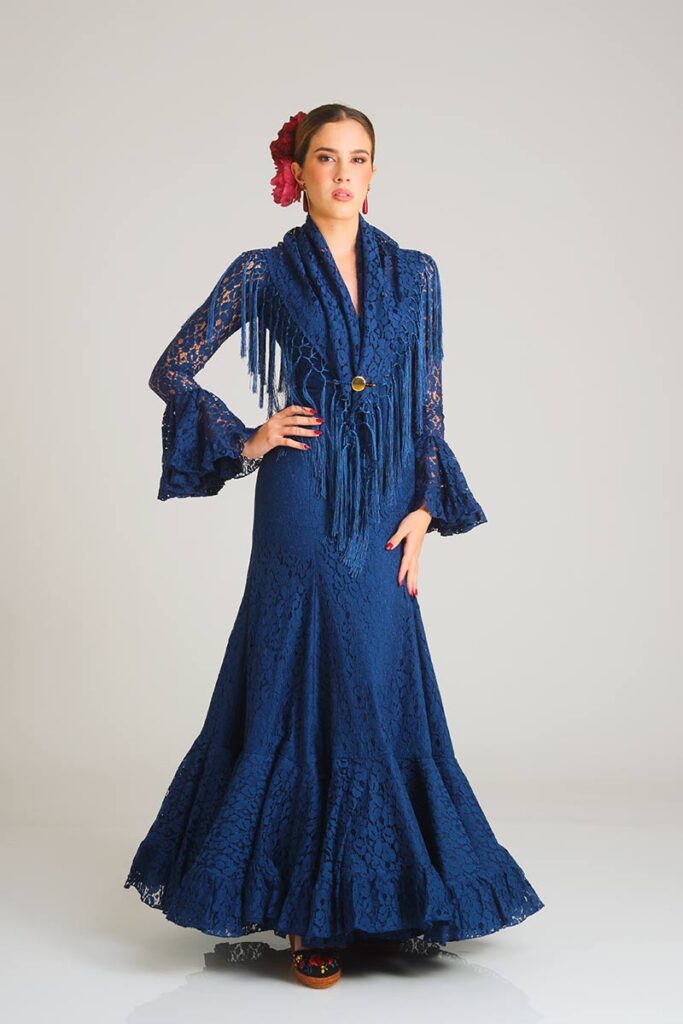 Traje de flamenca de alta costura en un profundo azul marino, diseñado con un delicado encaje floral, corte sirena ajustado y una falda estructurada con volantes que aporta elegancia y movimiento al conjunto.