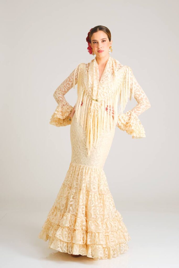 Traje de flamenca artesanal en tono crema confeccionado en encaje de motivos florales, con corte sirena ajustado y falda compuesta por múltiples niveles de volantes sutiles.