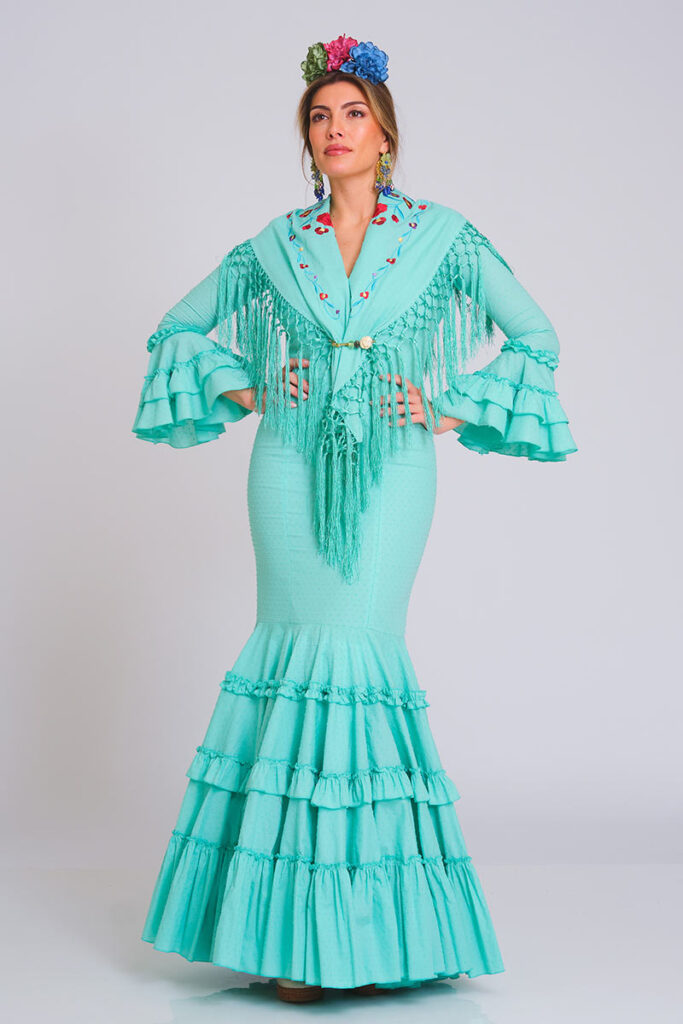 Vestido de flamenca en color verde agua con estampado de lunares en relieve, corte sirena y falda de volantes escalonados. Traje de gitana de diseño artesanal combinado con mantón bordado a juego con flecos largos. Mangas de doble volante. Perfecto para la Feria de Abril, romerías y eventos de moda flamenca