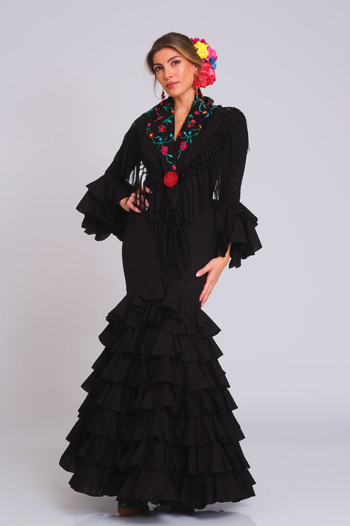 Vestido de flamenca negro con estampado de lunares y falda de volantes en cascada. Traje de gitana para mujer, diseño clásico de alta costura, combinado con mantoncillo bordado en tonos vivos y flecos largos. Mangas de doble volante. Perfecto para la Feria de Abril y eventos de moda flamenca