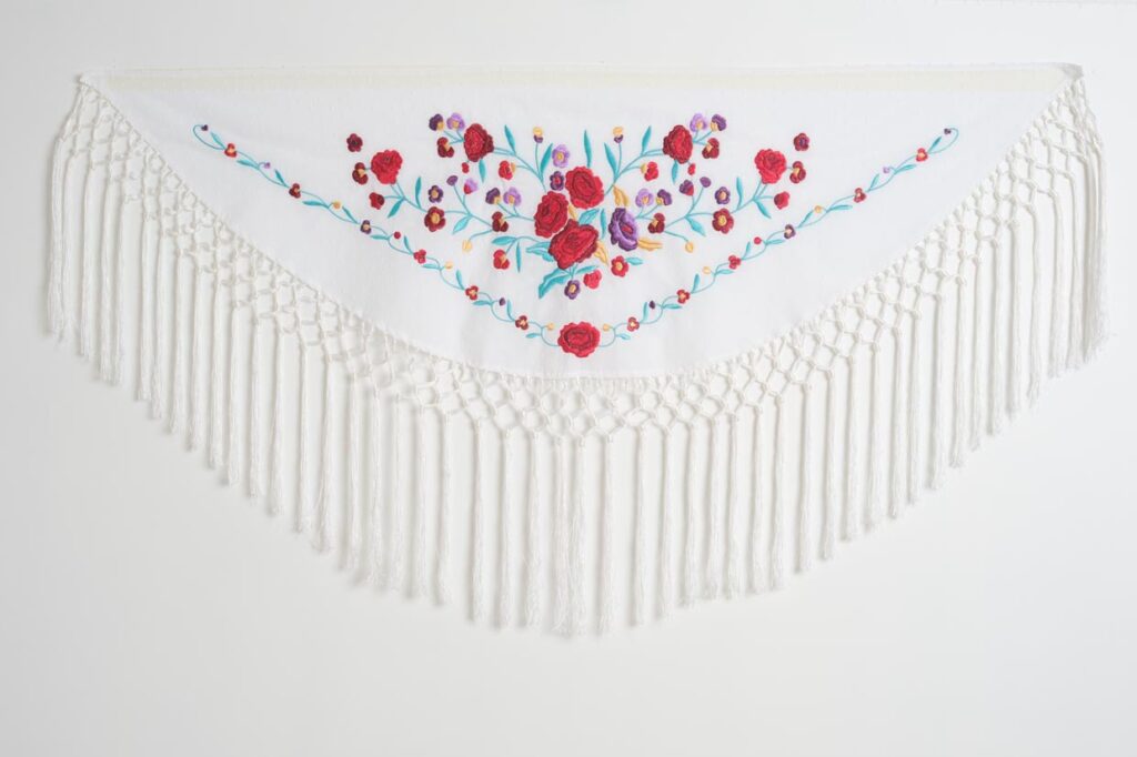 Mantón de flamenca triangular en color blanco con bordado floral de rosas y flecos largos anudados