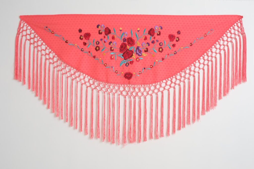 Mantón de flamenca triangular en color coral con bordado floral de rosas y flecos largos anudados