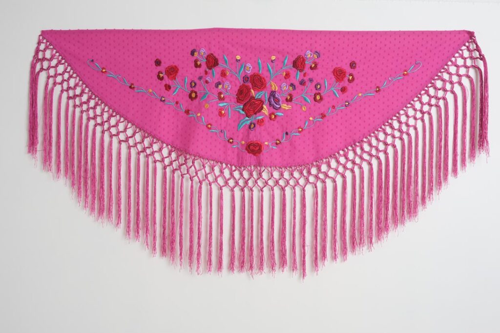 Mantón de flamenca triangular en color fucsia con bordado floral de rosas y flecos largos anudados