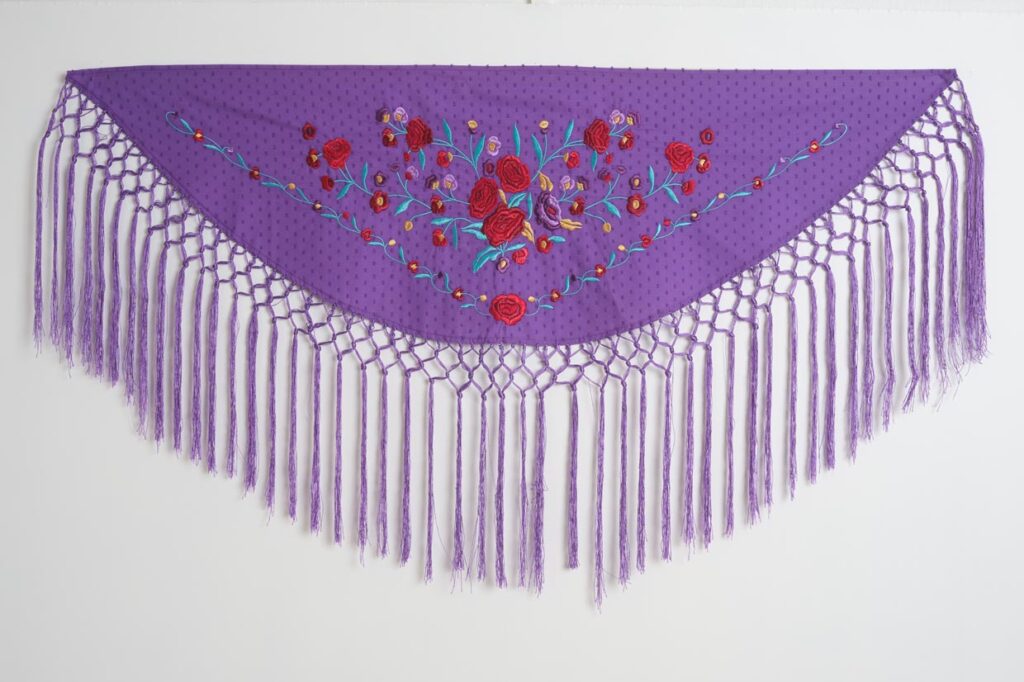 Mantón de flamenca triangular en color morado con bordado floral de rosas y flecos largos anudados
