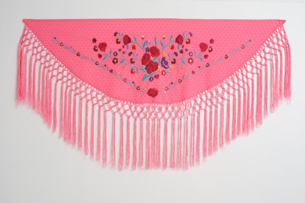 Mantón de flamenca triangular en color rosa vibrante con bordado floral de rosas y flecos largos anudados