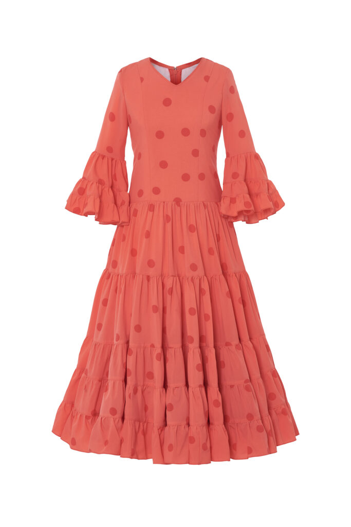 Llamativo traje de flamenca infantil en un tono coral con estampado de lunares, diseñado con un corte clásico que luce múltiples volantes en la falda y mangas para un movimiento espectacular, perfecto para celebraciones y eventos tradicionales