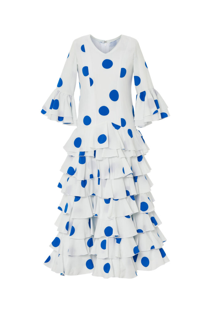 Vistoso traje de flamenca infantil en color blanco con lunares azules, diseñado con cuerpo entallado y falda de volantes escalonados que aportan gran movimiento, ideal para celebraciones y ferias andaluzas