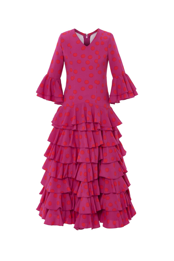 Llamativo traje de flamenca infantil en color fucsia con estampado de lunares, diseñado con un corte clásico que luce múltiples volantes en la falda y mangas para un movimiento espectacular, perfecto para celebraciones y eventos tradicionales