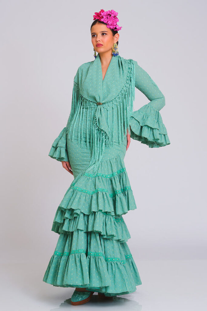 Encantador traje de flamenca en un suave tono verde agua con sutiles detalles bordados, confeccionado con un diseño ajustado que fluye en volantes asimétricos, ideal para destacar con un estilo fresco y tradicional en las ferias andaluzas