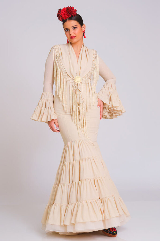 Traje de flamenca en un elegante tono beige con un sutil estampado de lunares, que resalta por su diseño ajustado y la estructura clásica de volantes en las mangas y la falda, ideal para proyectar un estilo atemporal y refinado en cualquier evento andaluz
