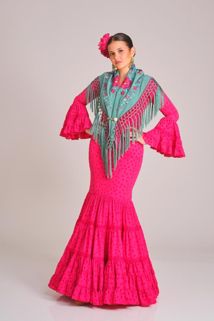 Vestido de flamenca en un vibrante tono fucsia con estampado de lunares, que destaca por su silueta ceñida y la estructura de volantes en mangas y falda