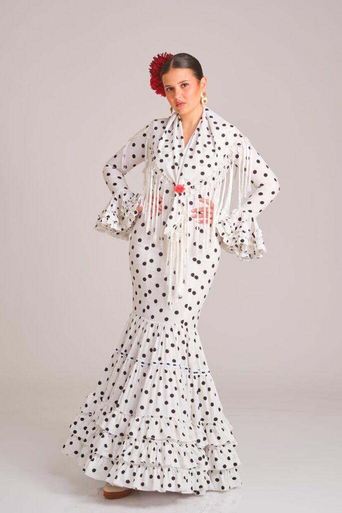 Traje de flamenca blanco con lunares negros, diseño entallado con volantes en la falda y mangas, incluye mantoncillo con flecos a juego