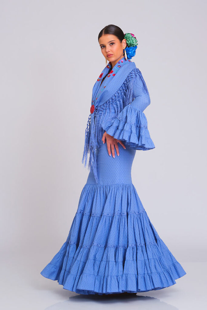 Traje de flamenca azul elegante con manton de flecos y falda con pliegues, una opción moderna y colorida para la feria