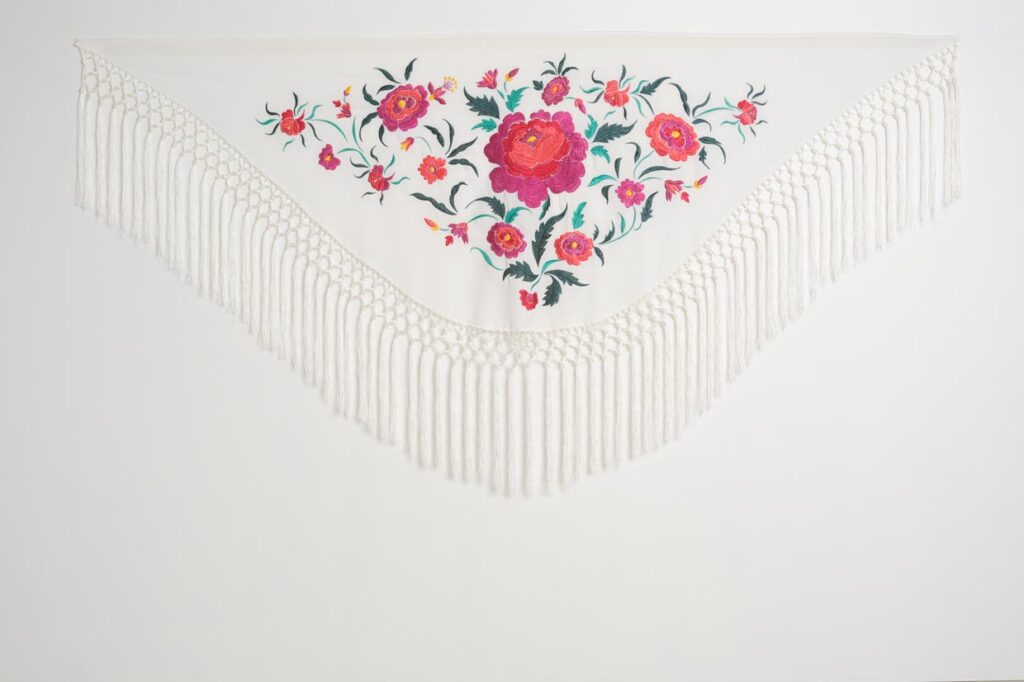 Mantón blanco para traje de flamenca con flores fucsias y coral bordadas, hojas verdes y flecos largos de macramé
