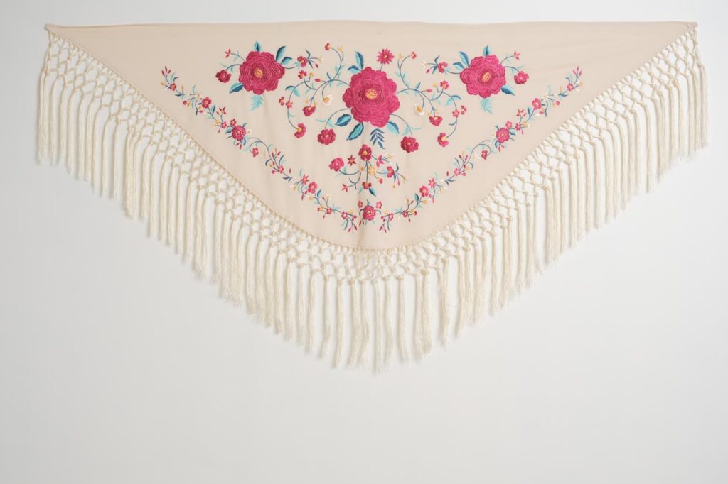 Mantón color marfil para traje de flamenca con rosas fucsias bordadas, hojas turquesa y flecos largos anudados
