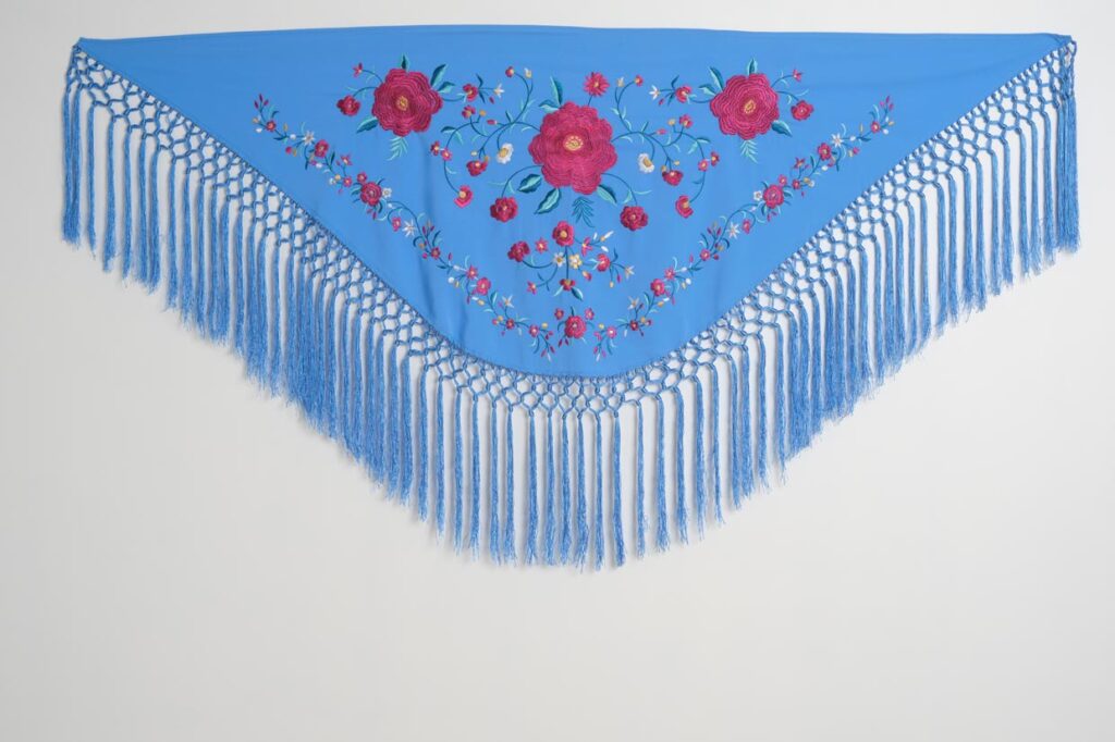 Mantón azul cielo para vestido de flamenca con rosas fucsias bordadas, motivos florales y flecos largos anudados