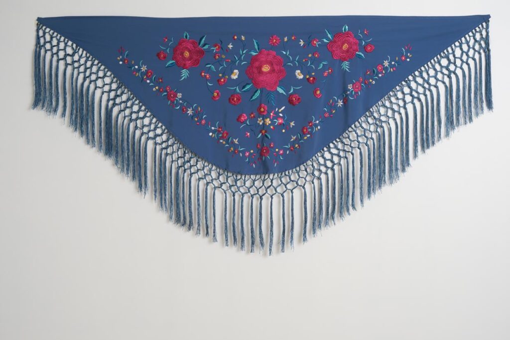 Mantón azul acero para traje de flamenca con rosas fucsias bordadas, detalles florales y flecos de rejilla largos