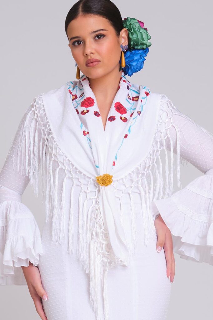 Look de flamenca blanco con mantoncillo bordado de rosas rojas, flecos largos y mangas de volantes