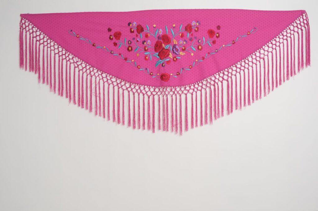 Mantoncillo flamenco fucsia con bordado de rosas rojas, detalles turquesa y flecos largos de macramé