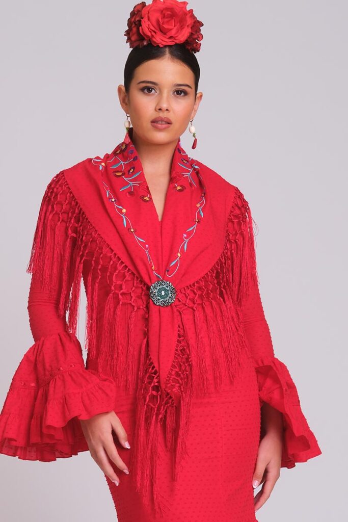 Vestido de flamenca rojo con mantoncillo bordado, flecos de rejilla, mangas con volantes y flor roja en el cabello