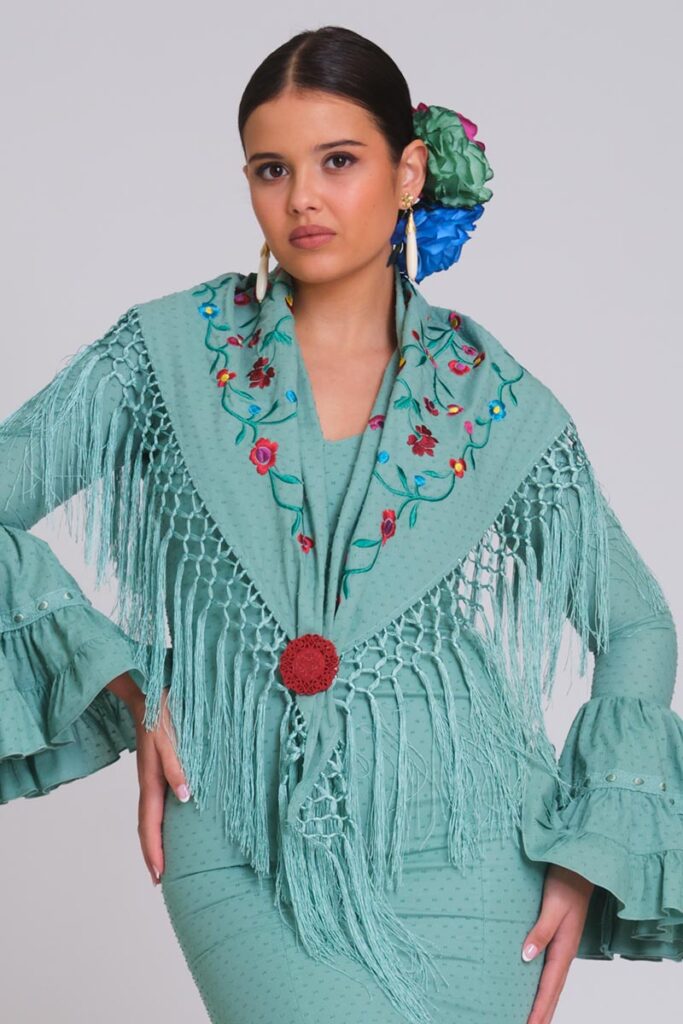 Modelo con traje de flamenca verde agua, mantón floral bordado con flecos largos y flores en el cabello