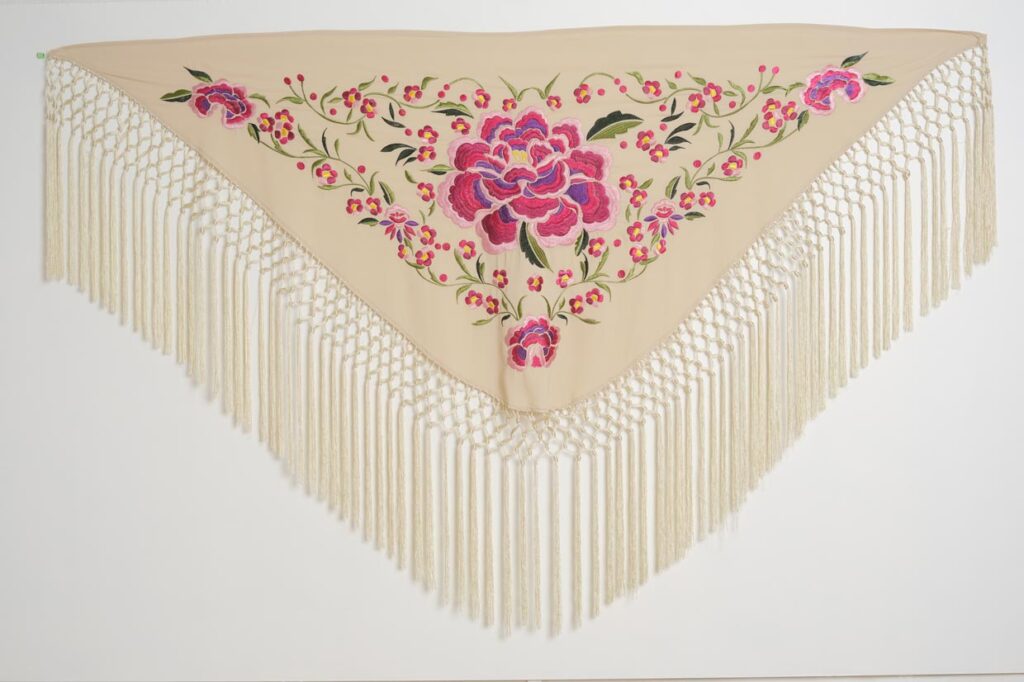 Mantón color marfil para feria con gran flor rosa bordada, detalles vegetales y flecos artesanales largos