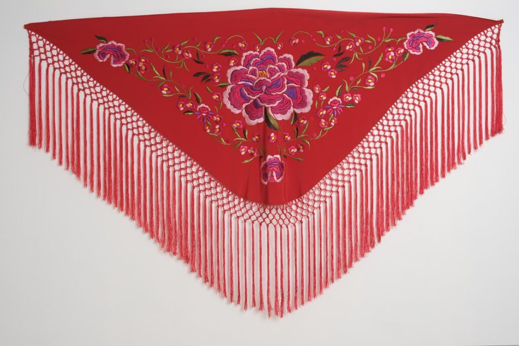 Mantón rojo para traje de flamenca con peonías rosas bordadas, motivos florales y flecos de macramé