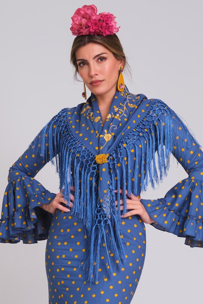 Vestido de flamenca azul azafata con lunares amarillo mostaza, mangas con volantes múltiples y mantoncillo bordado a juego con flecos.