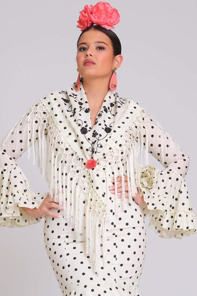Vestido de flamenca blanco con lunares negros, mangas de volantes múltiples y mantoncillo bordado con flecos blancos.