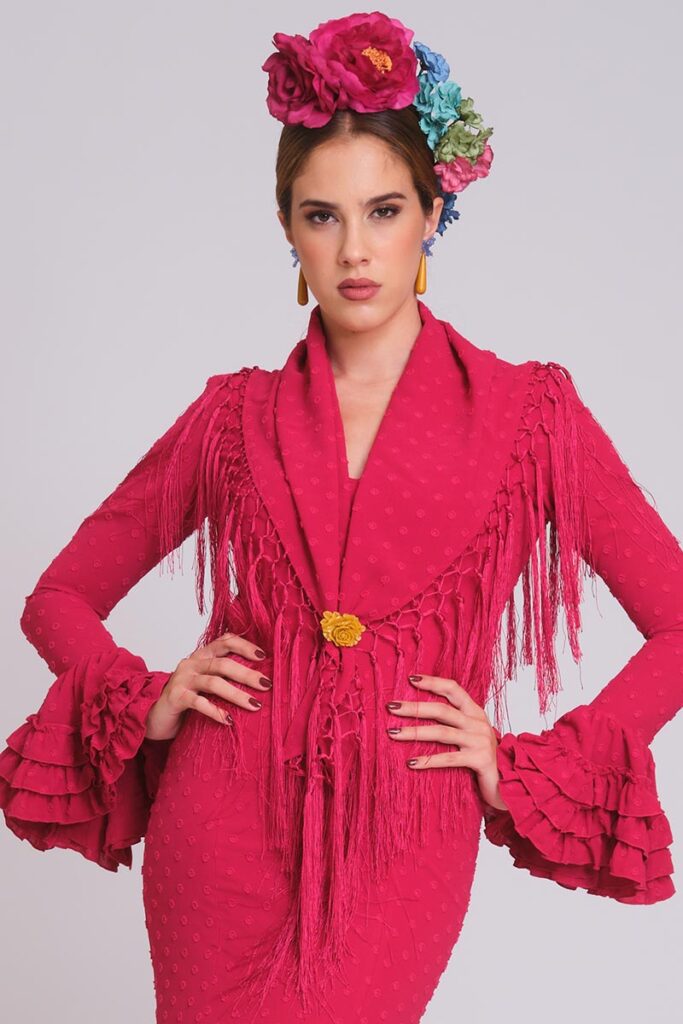Vestido de flamenca rosa fucsia de plumeti con relieve, mangas de volantes múltiples y mantoncillo de flecos largos magenta.