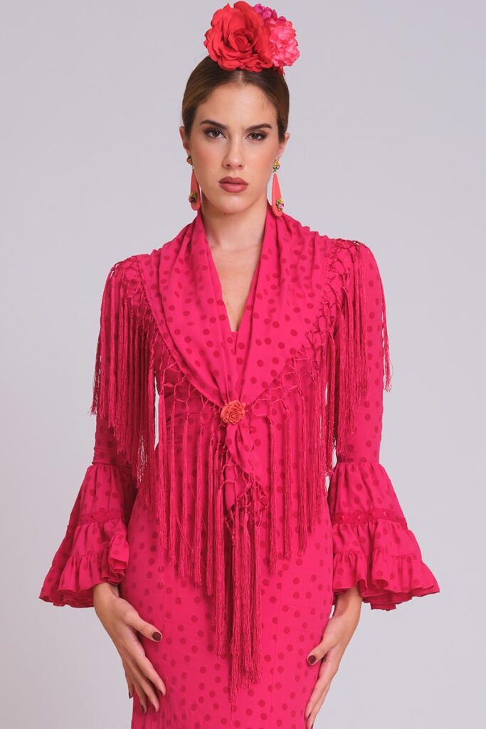 Vestido de flamenca rosa fucsia con lunares medianos al tono, mangas con volantes dobles y mantoncillo de flecos fucsia largo.