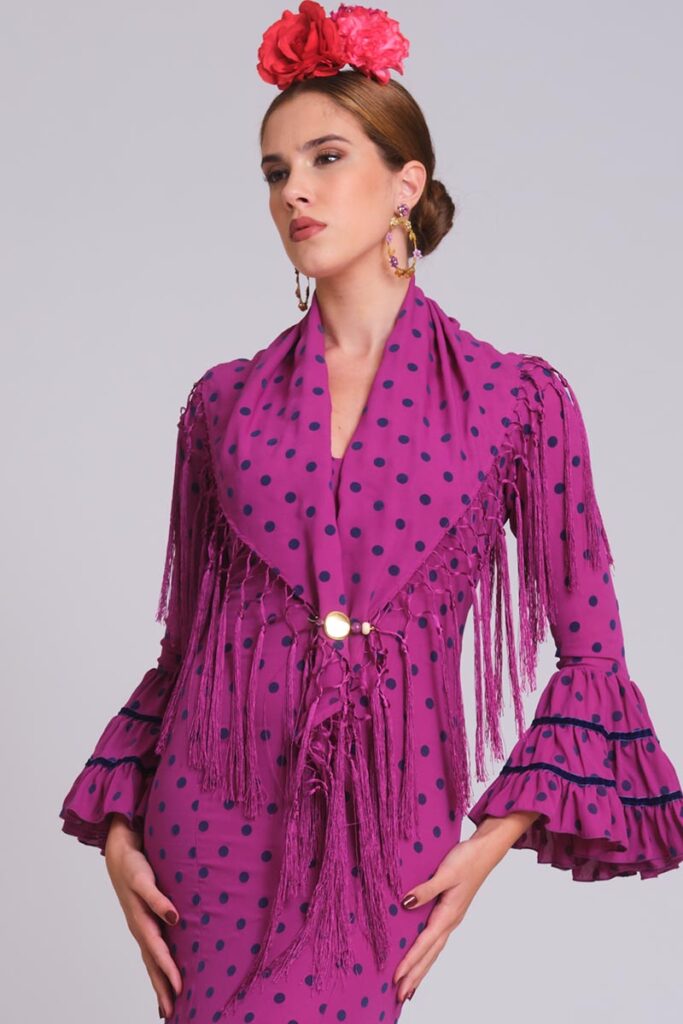 Vestido de flamenca buganvilla con lunares azul marino, mangas de volantes con terciopelo y mantoncillo de flecos a juego.
